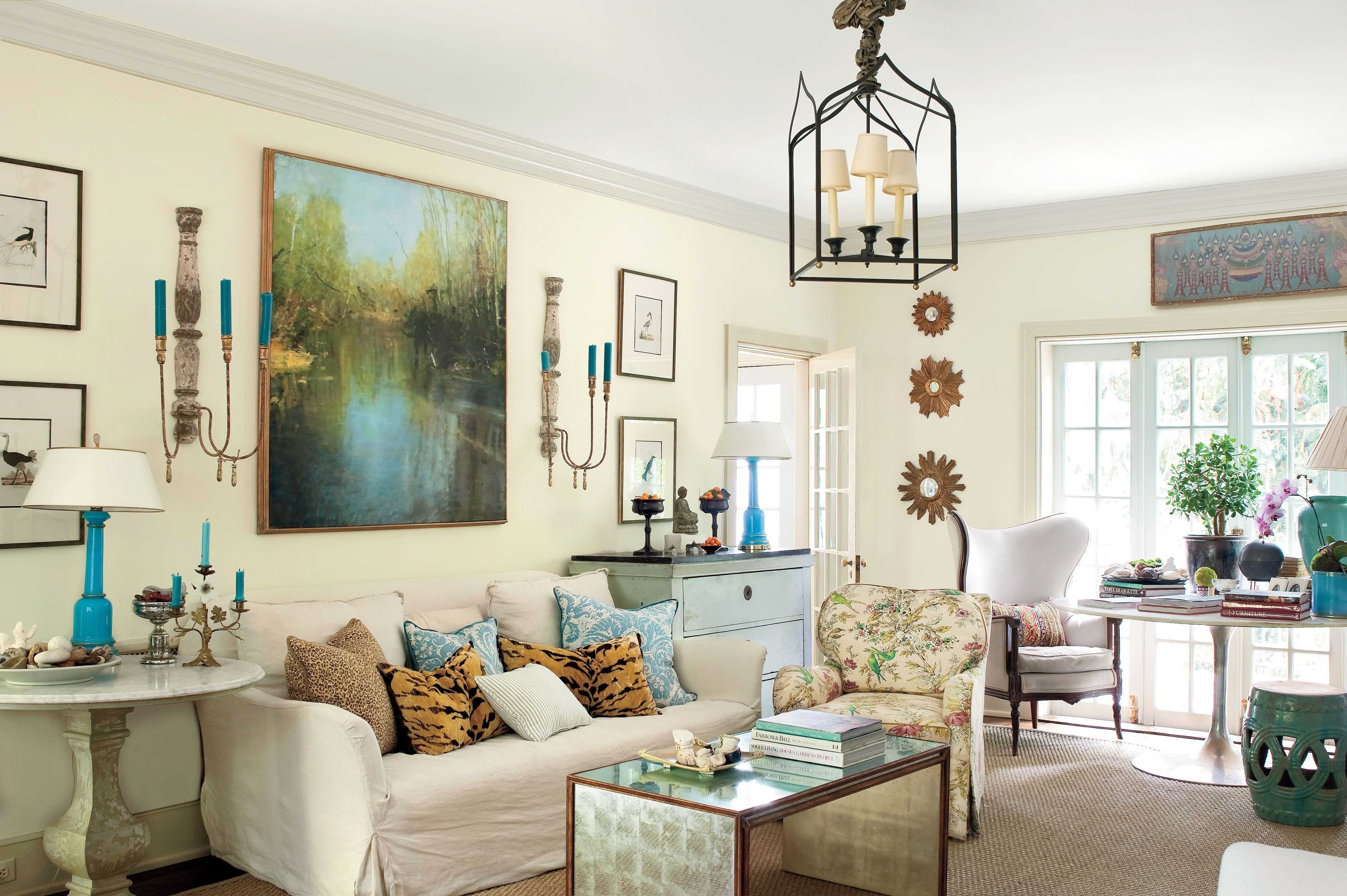Elegant living room with a cream sofa accented by animal-print and blue patterned pillows, a large landscape painting above, and blue table lamps on side tables