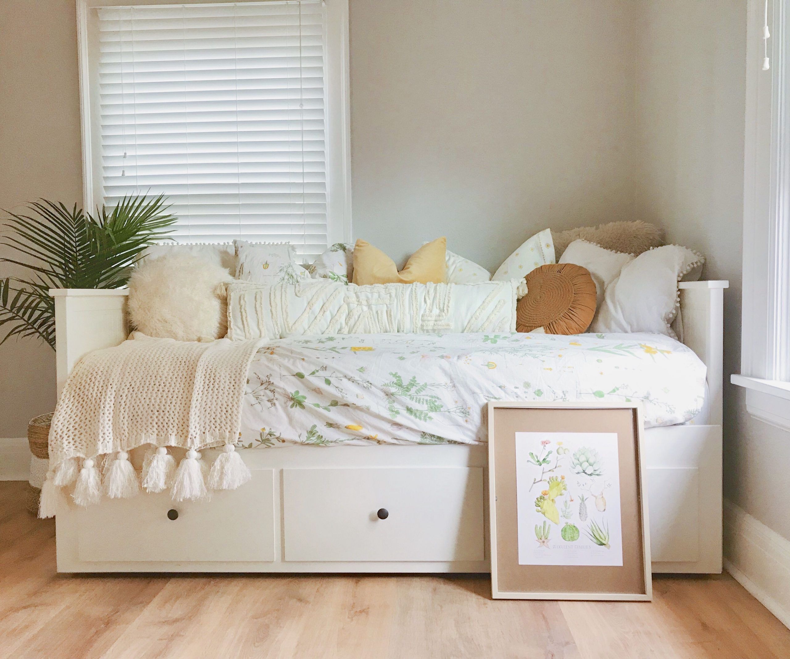 Cozy bedroom corner with a white daybed with storage drawers, floral bedding, assorted cream and yellow pillows, and a knit throw