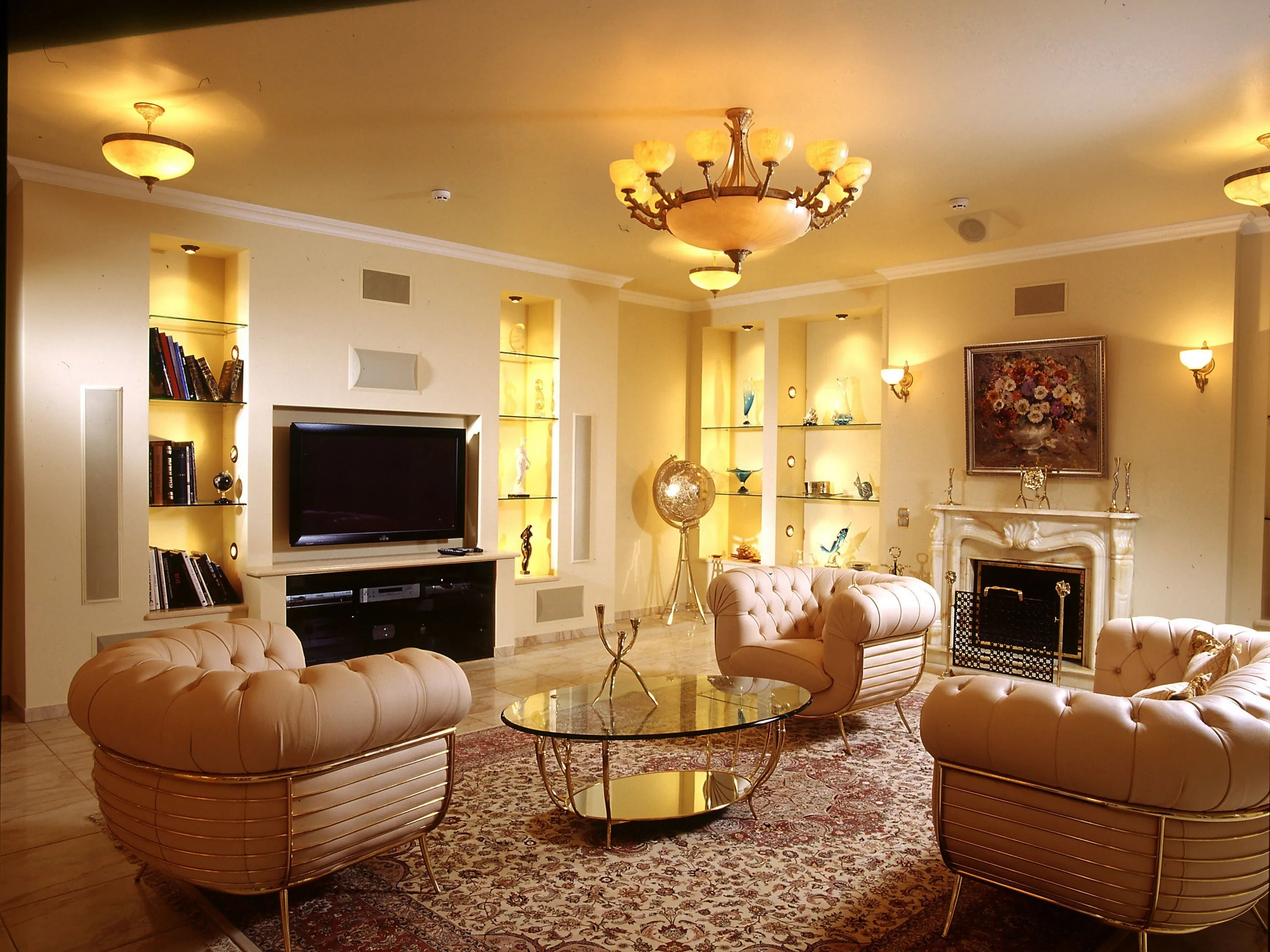 Opulent living room with cream tufted leather armchairs, a round glass and gold coffee table, patterned rug, and marble fireplace