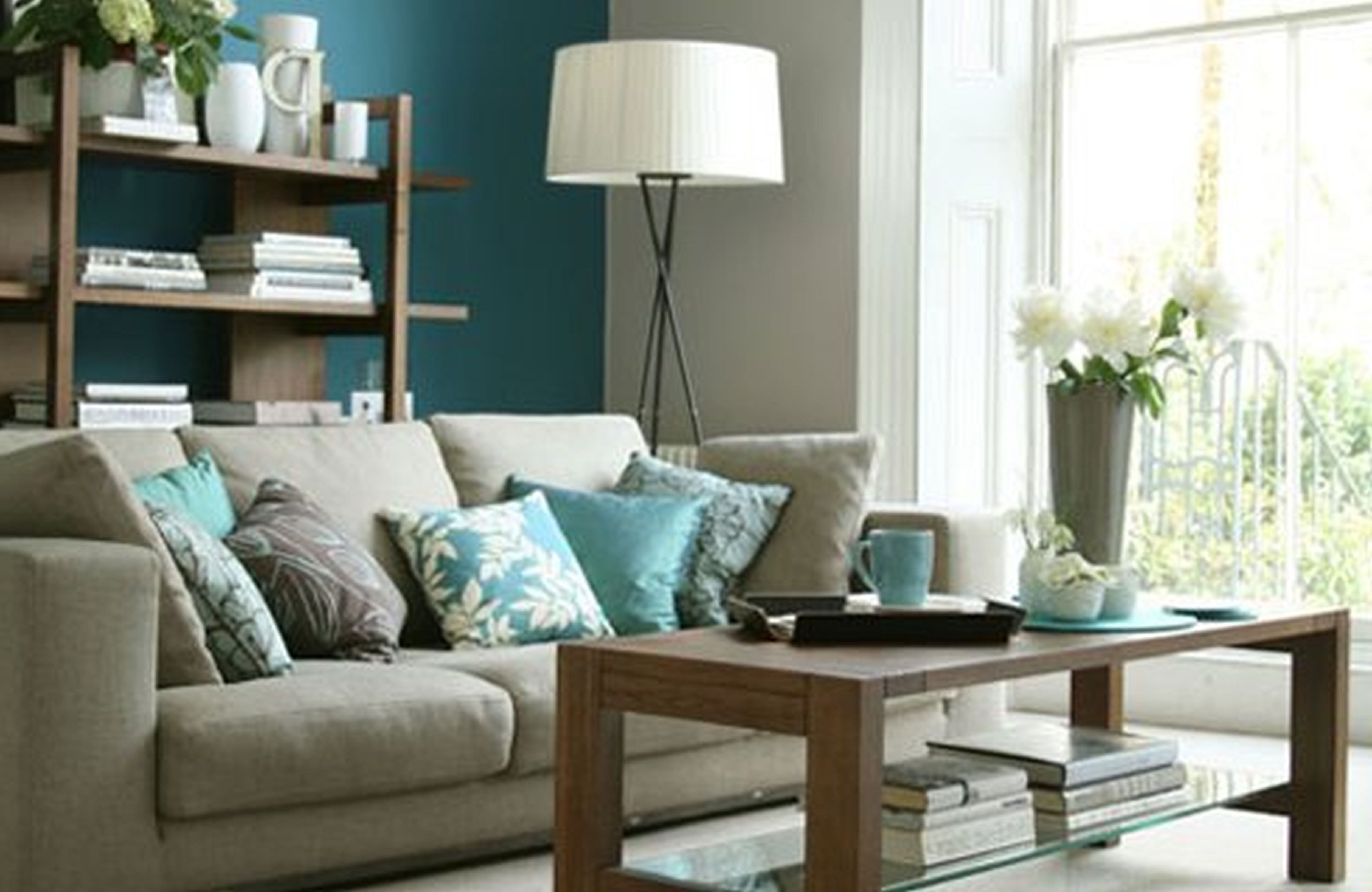 Cozy living room corner with teal accent wall, beige sofa with turquoise pillows, and wooden coffee table near bright window