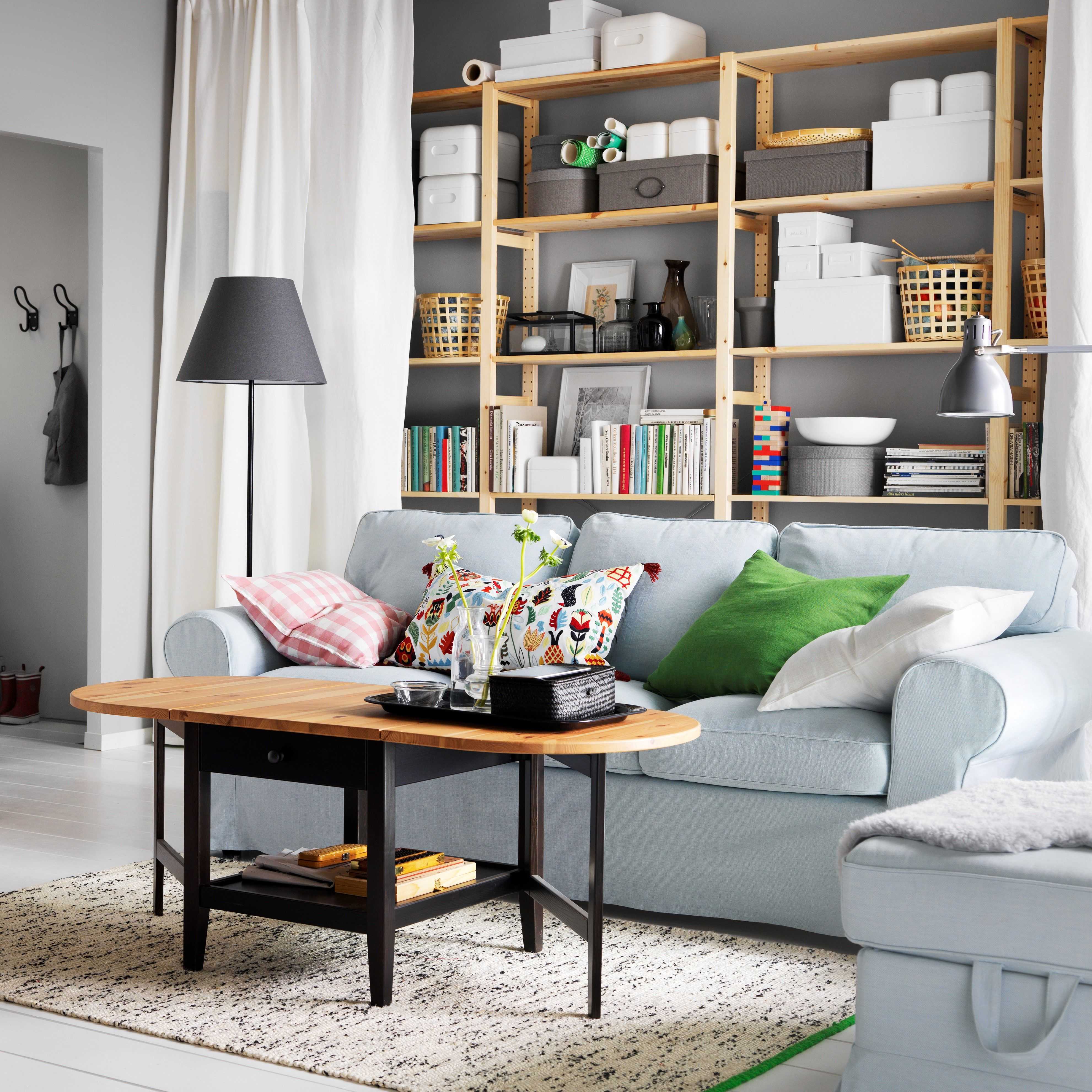Living room with pale blue sofa, colorful throw pillows, wooden shelving unit filled with storage boxes and books