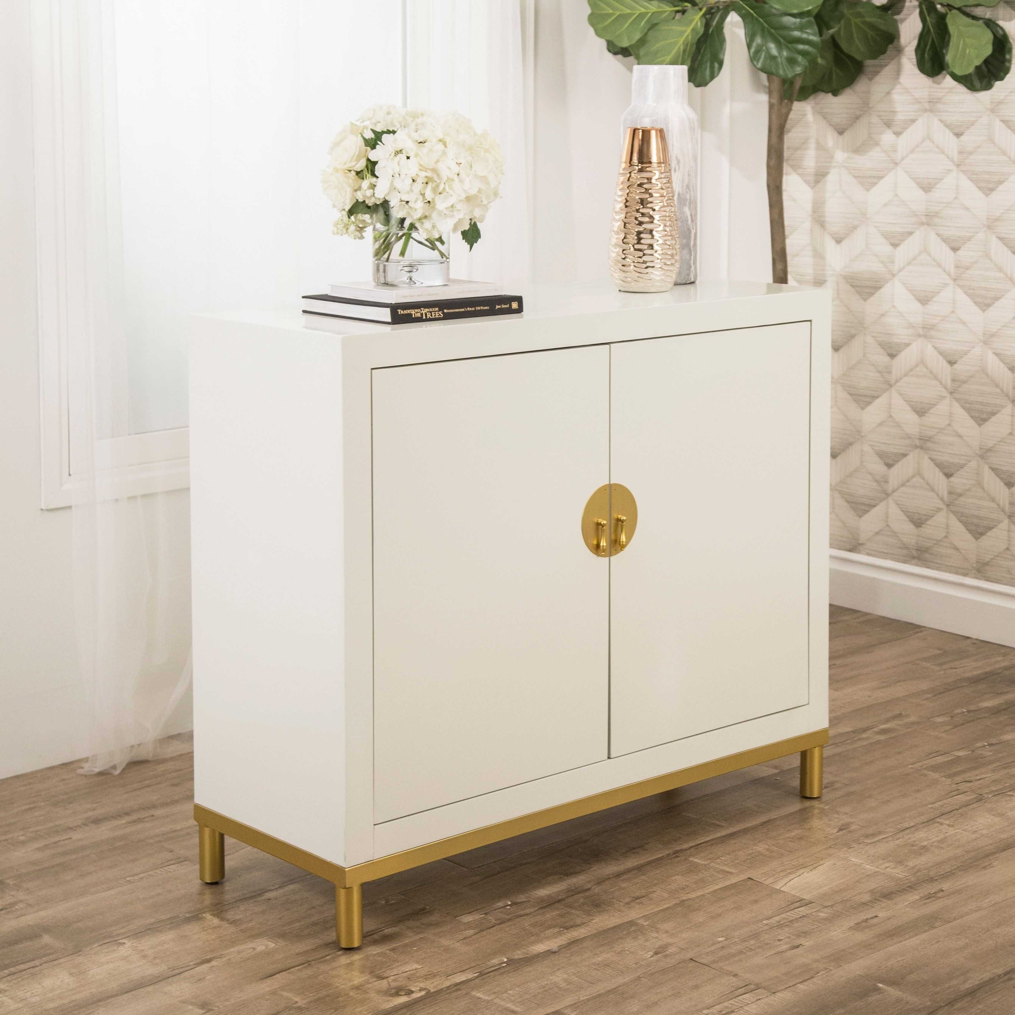 White lacquered cabinet with gold hardware and legs, styled with a flower arrangement, decorative vase, and stacked book