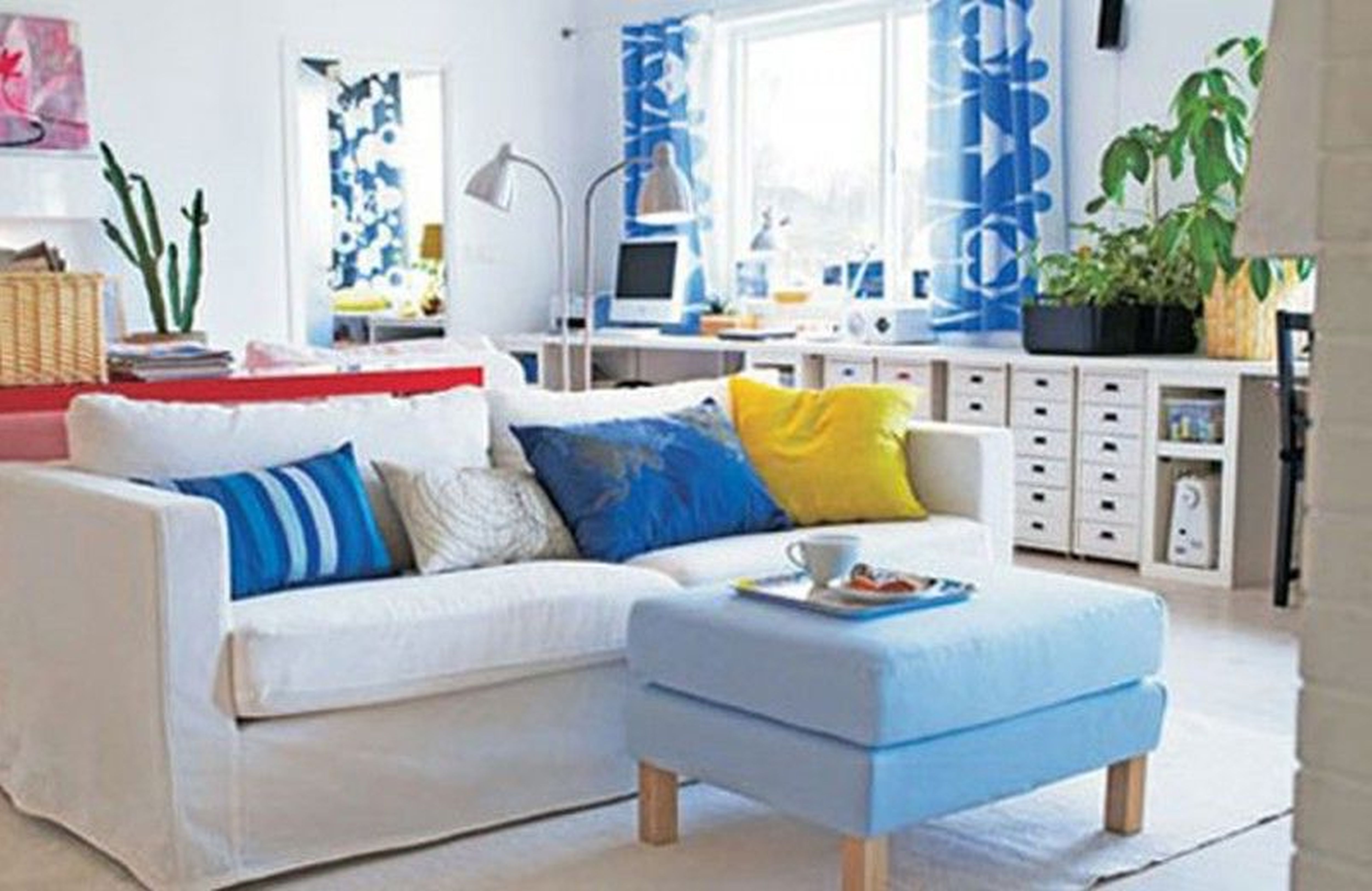 Airy living room with white sofa, blue and yellow pillows, blue patterned curtains, and light blue ottoman