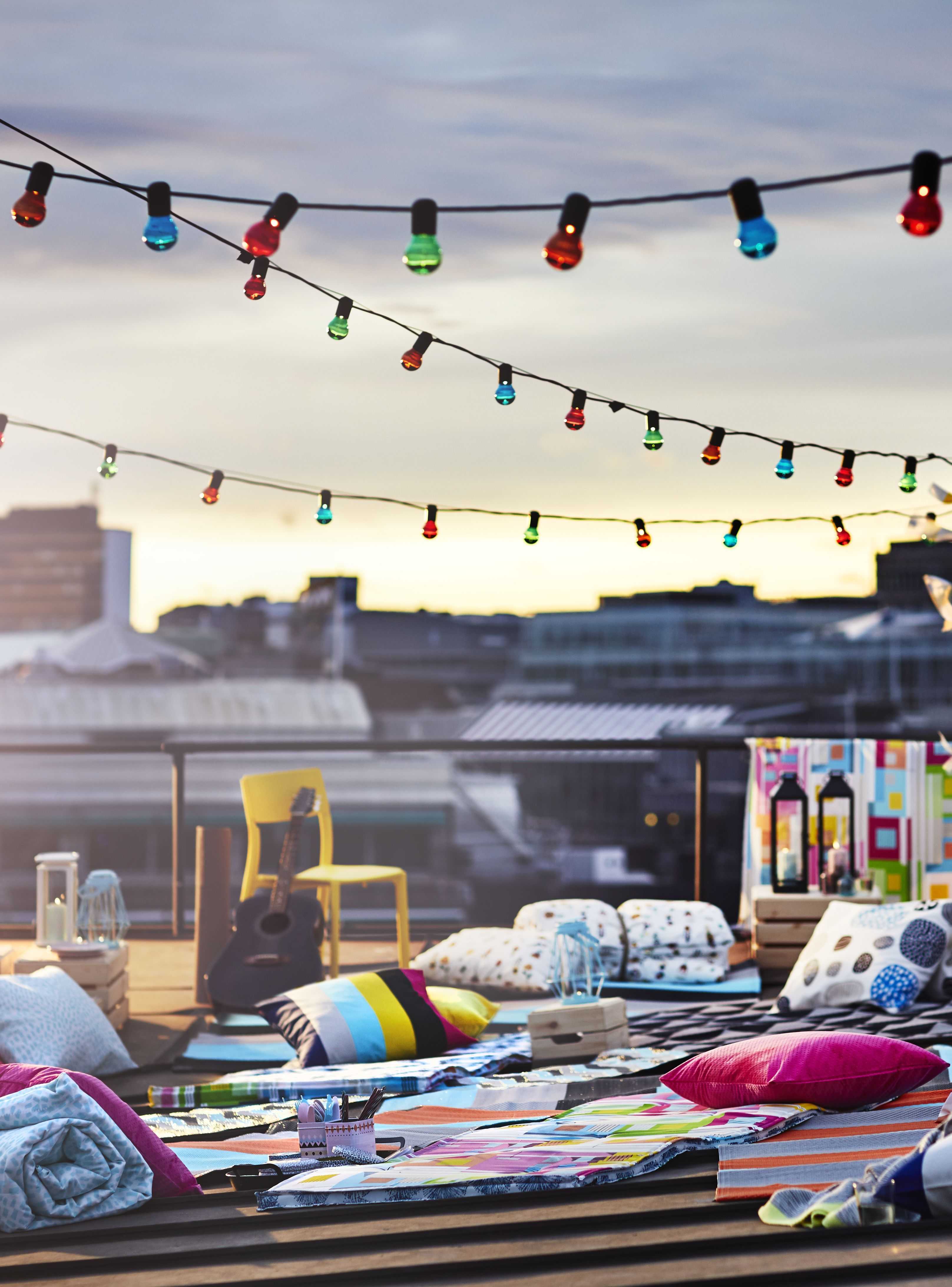 Rooftop terrace at dusk with warm string lights, colorful cushions and blankets, and a relaxed bohemian atmosphere