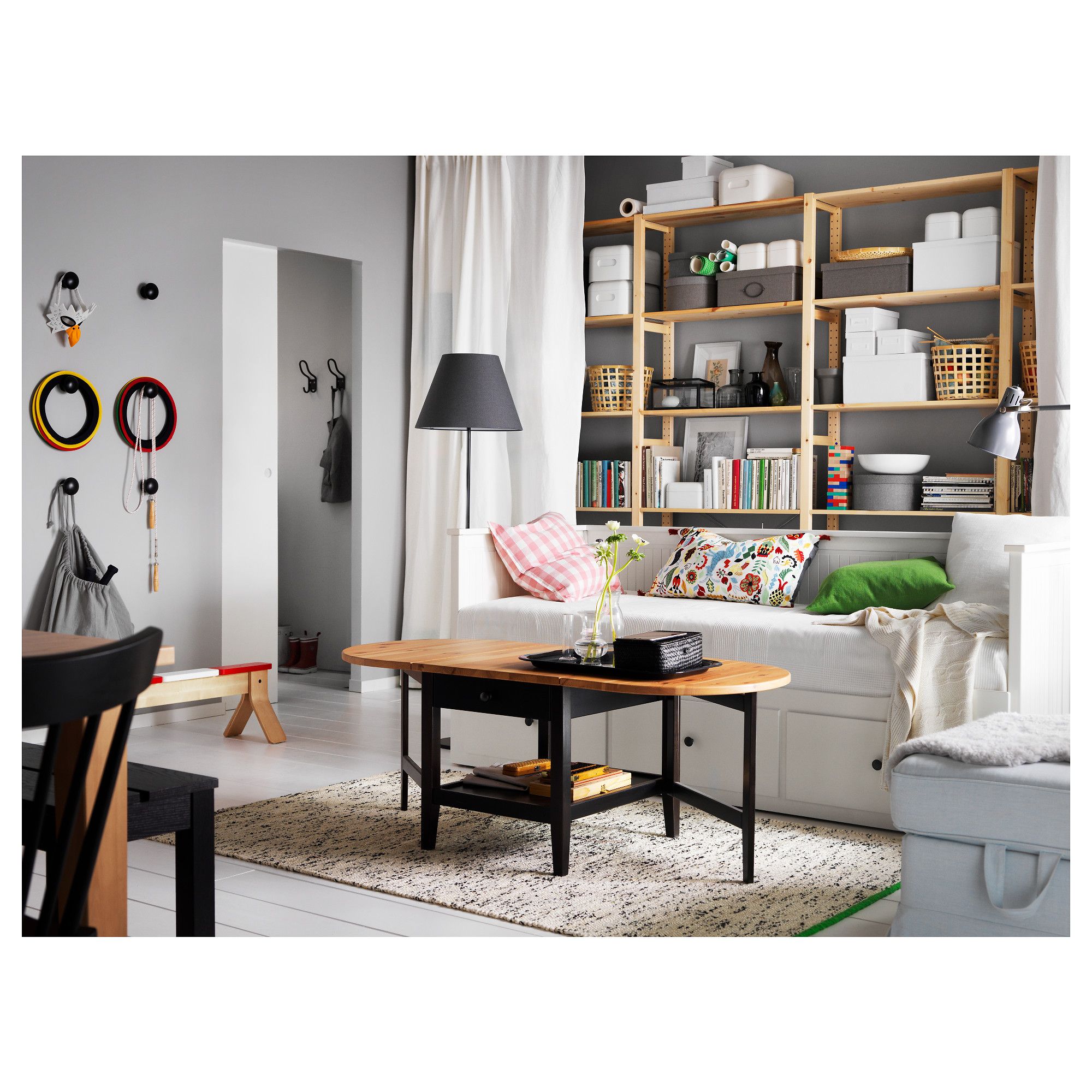 Living room with wooden shelving unit filled with storage boxes and books, a round wood and black coffee table, white daybed