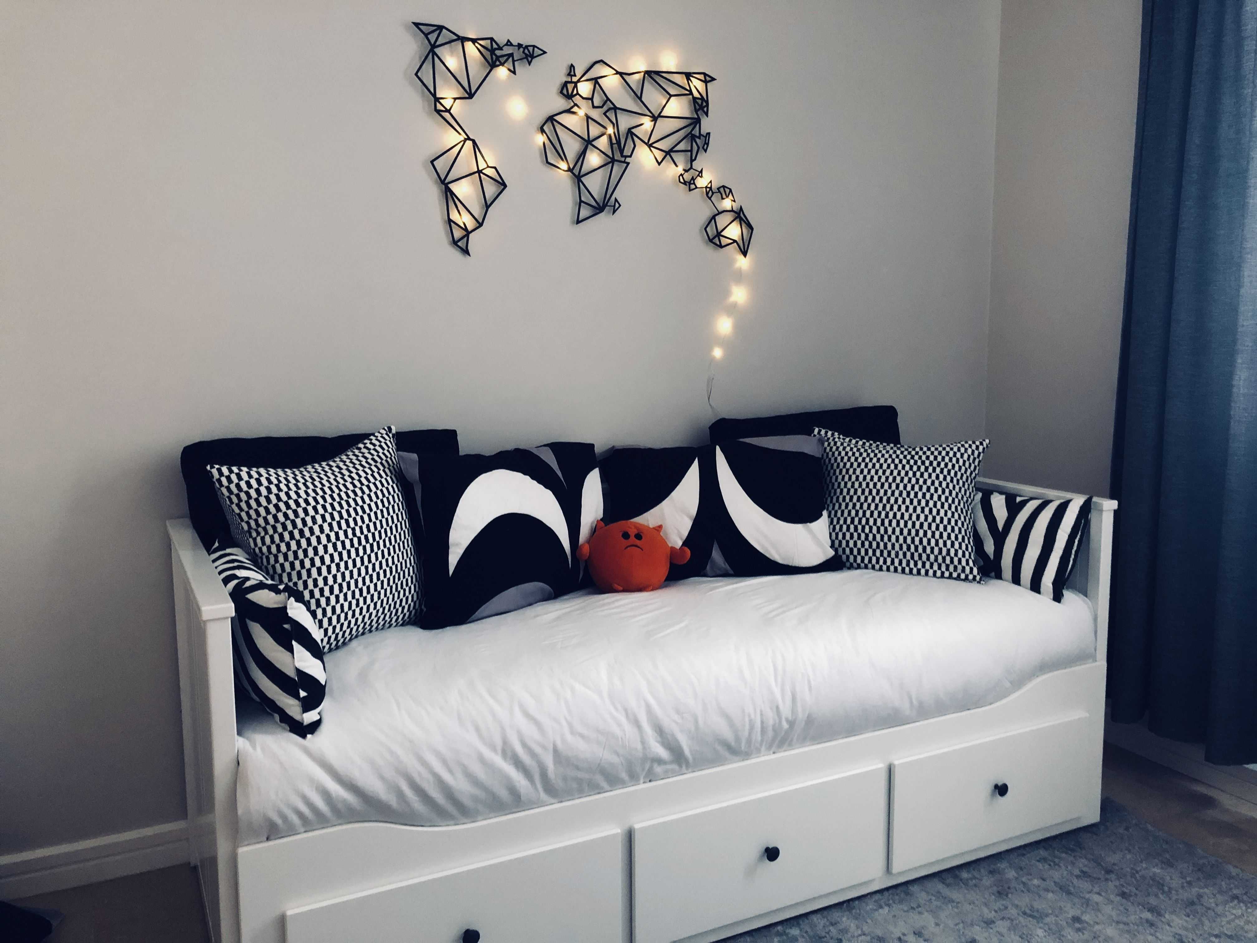 Bedroom daybed with white bedding and black-and-white patterned throw pillows, an orange plush toy, and a geometric wall